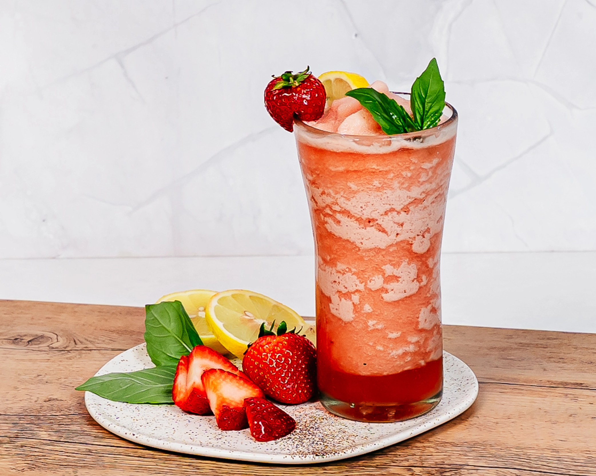 Strawberry lemonade slush garnished with fresh strawberries, lemon slices, and basil leaves, served in a tall glass.
