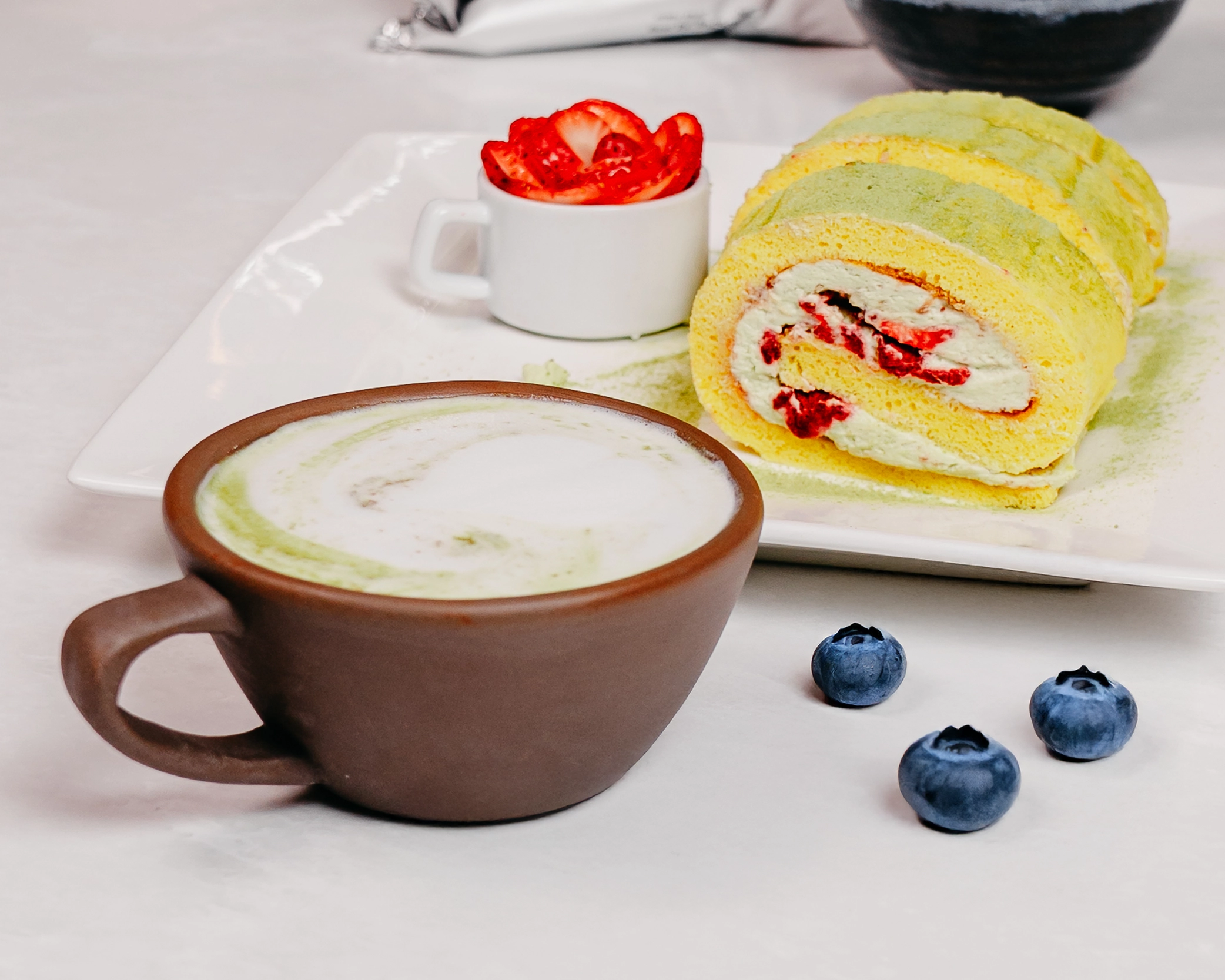 A hot matcha latte served in a brown ceramic mug and staged with blueberries.