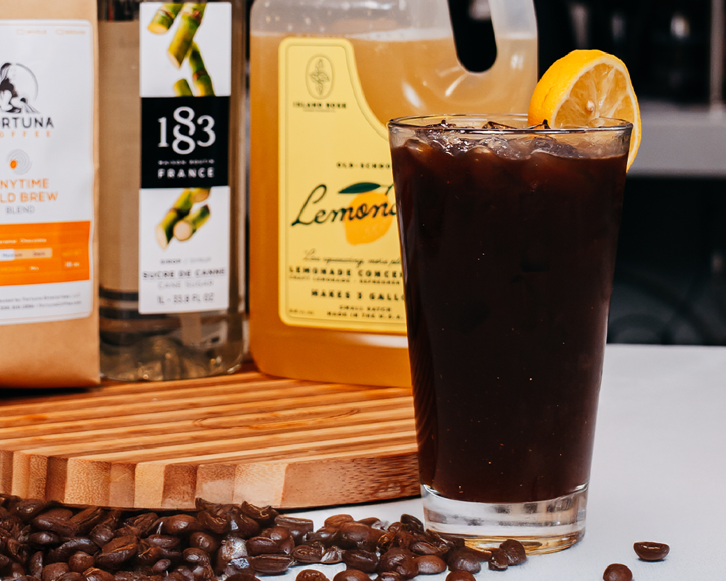 Iced lemonade drink in a clear glass with citrus garnishes, styled with syrup bottles in the background.