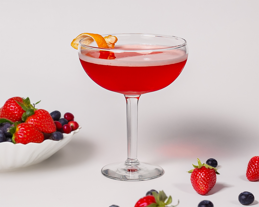 Pale pink mocktail in a tall glass with citrus and cranberry accents.