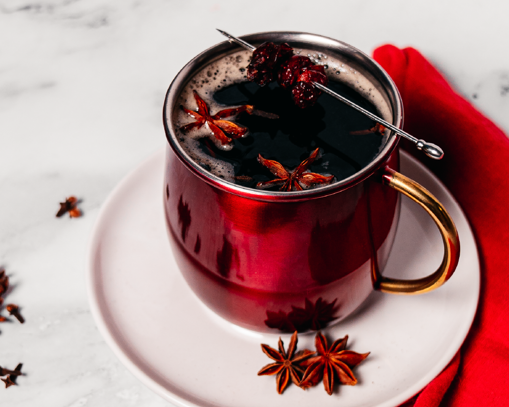 Hot cranberry apple cider in a red mug, garnished with star anise and berries on a white surface.