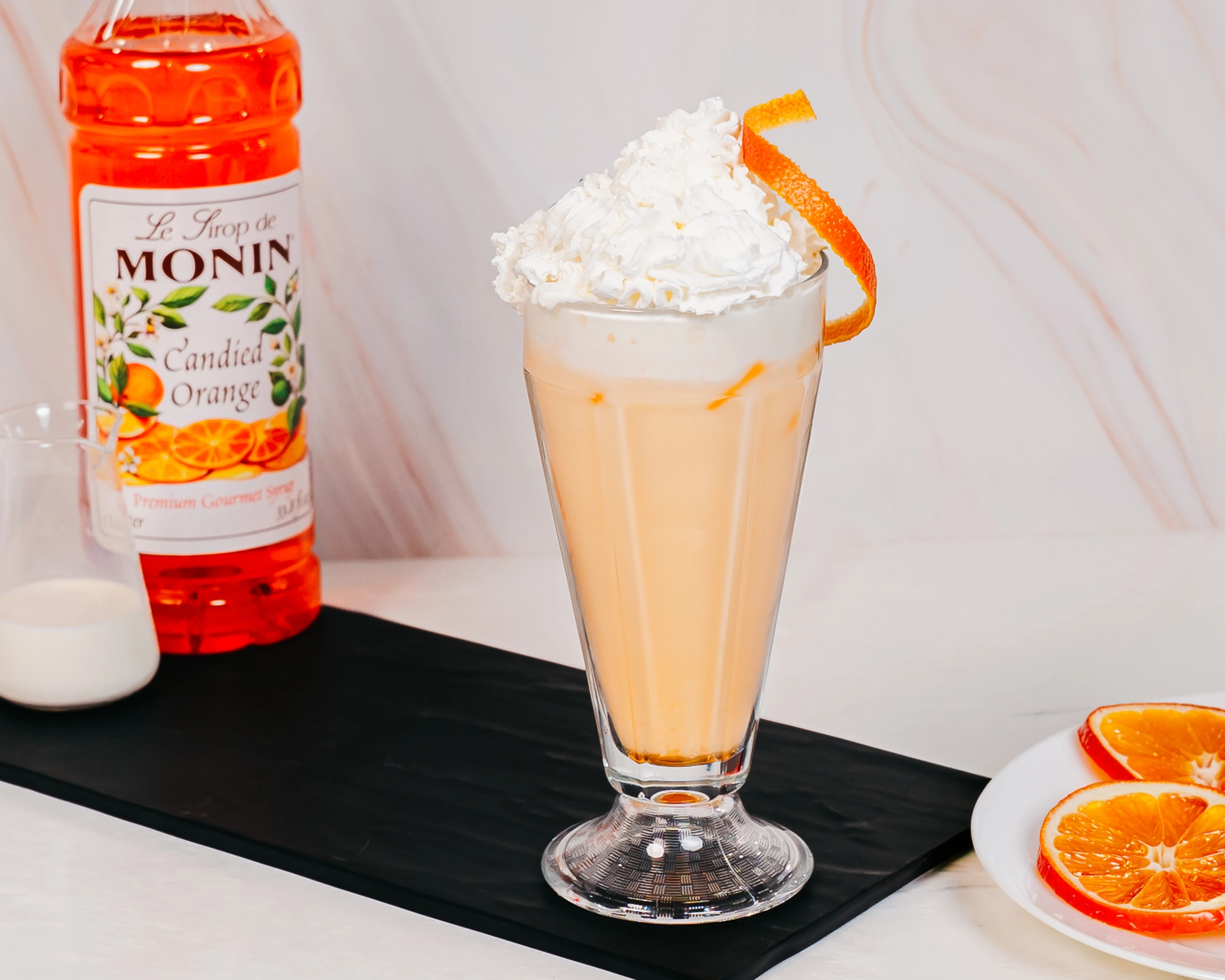 Creamy Candied Orange iced beverage topped with whipped cream and an orange twist, served in
