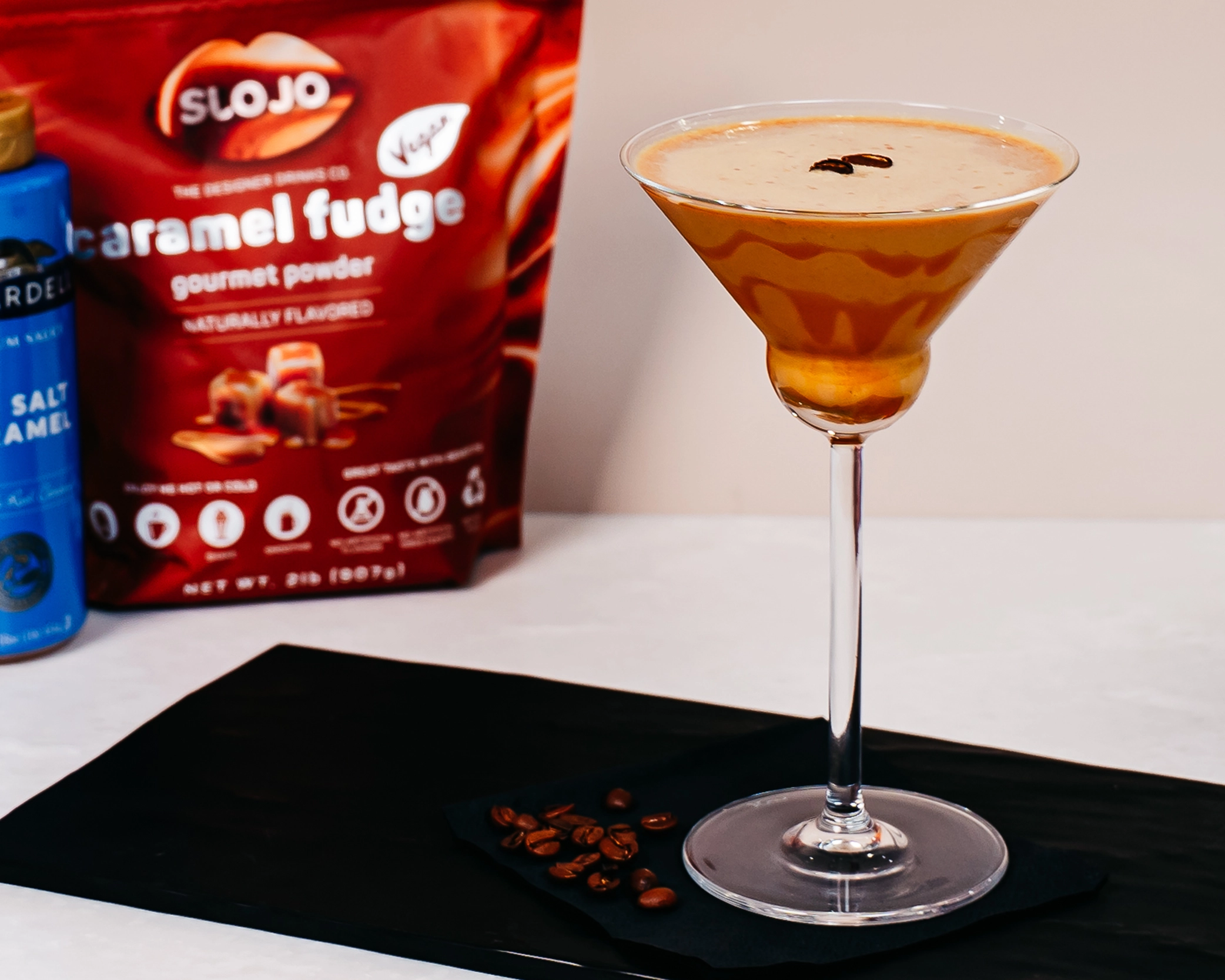 Caramel Fudge vegan mocktini made with SloJo gourmet powder, served in a martini glass with espresso beans on  black serving board.