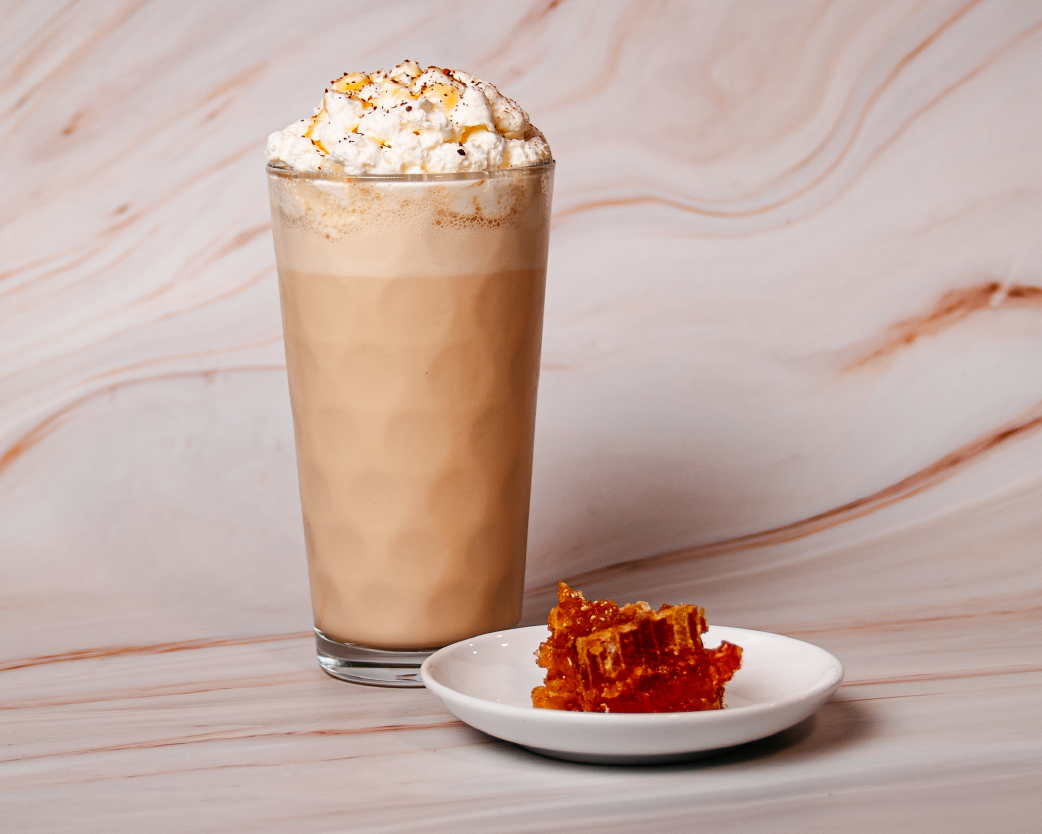 Creamy milkshake topped with whipped cream in a tall glass, served with a honeycomb garnish on a marble surface.
