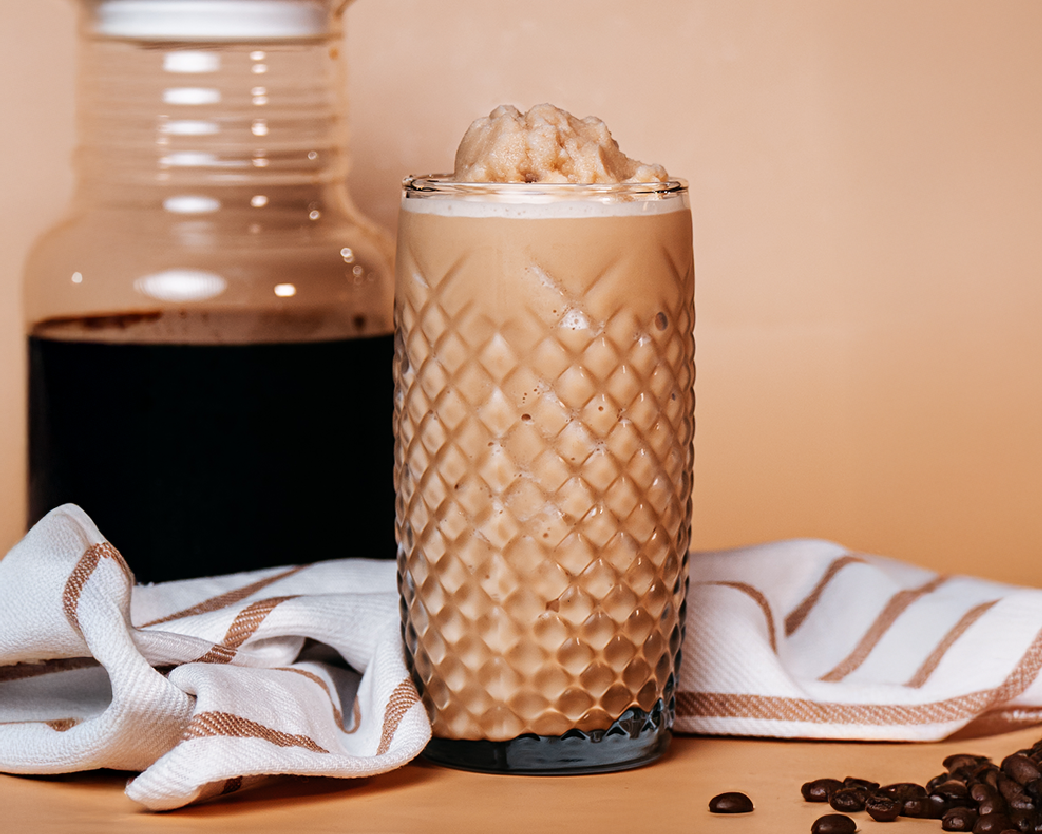 Icy cold brew beverage in a tall glass with foam and ice.