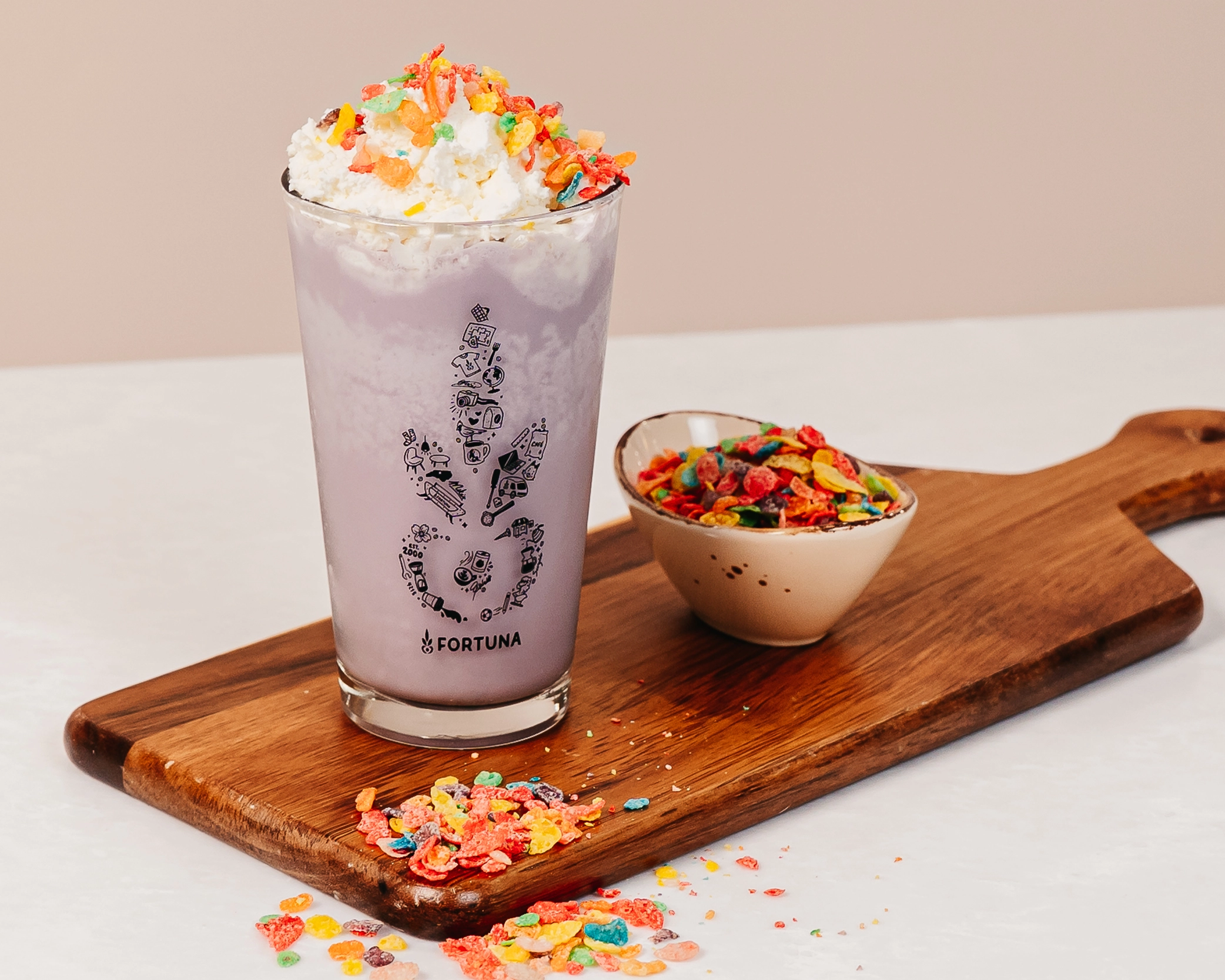 Lavender White Chocolate frappe topped with whipped cream and fruity cereal pieces, served on a wooden board with a bowl of colorful cereal.