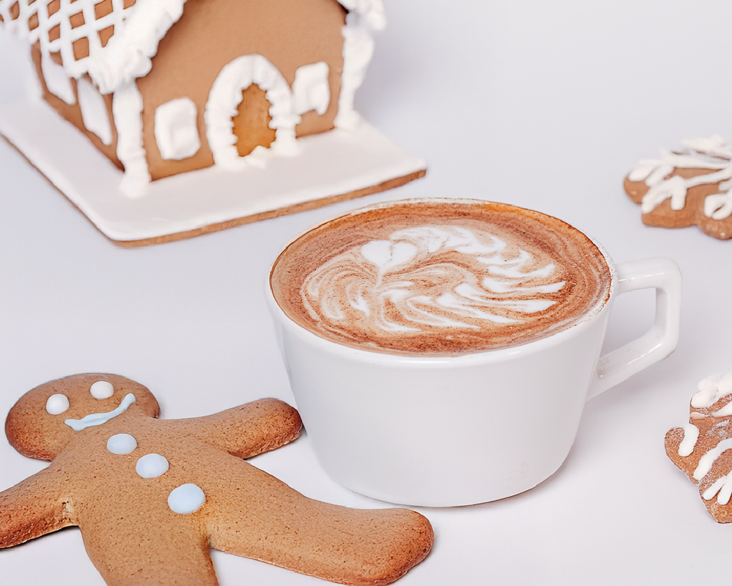Hot latte in a white cup with latte art, styled with gingerbread cookies and a festive white backdrop.