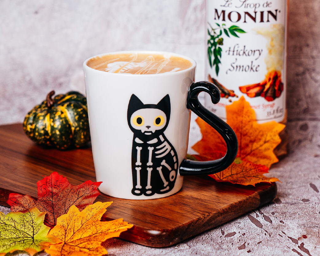 Hot latte in a seasonal mug with autumn leaves and a syrup bottle styled in the background.