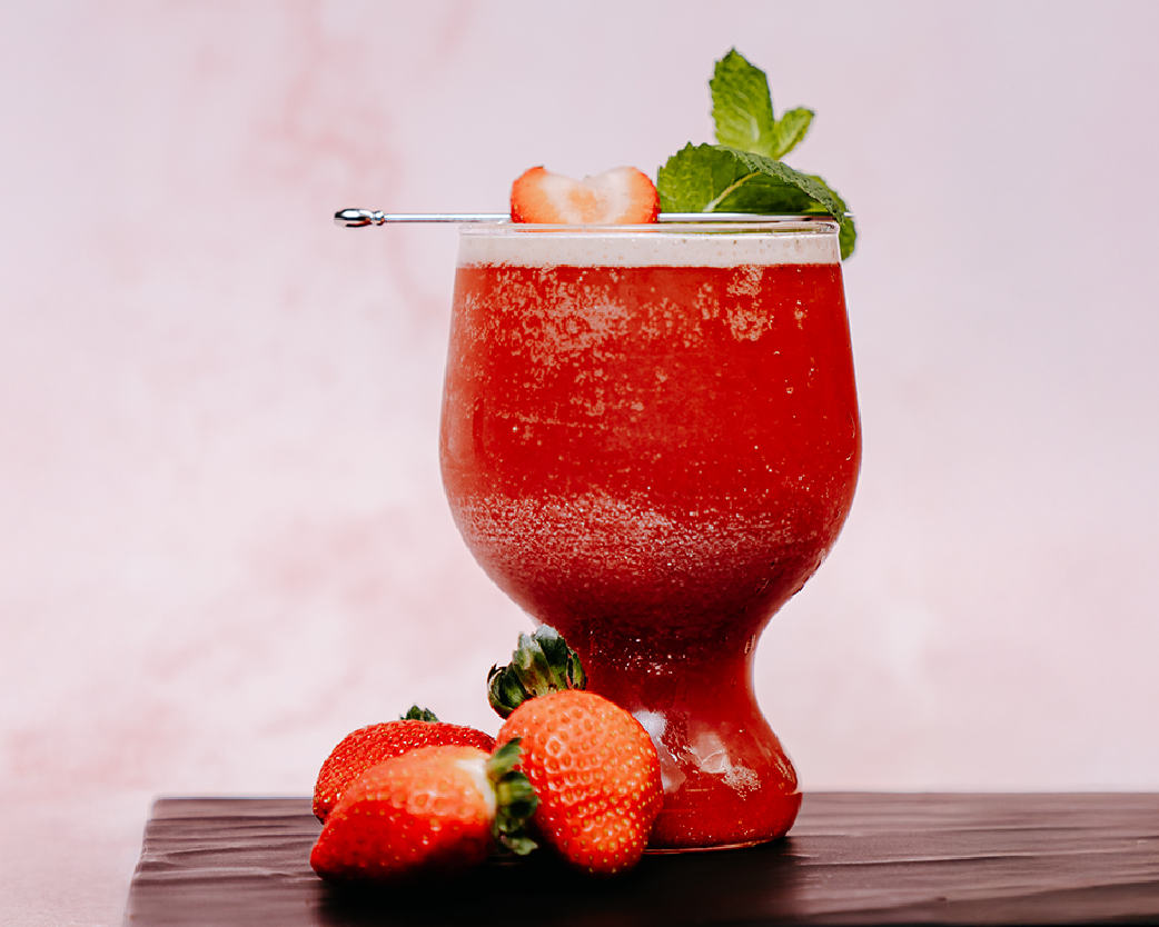 Chilled red beverage in a curved glass, garnished with fresh strawberries and mint.