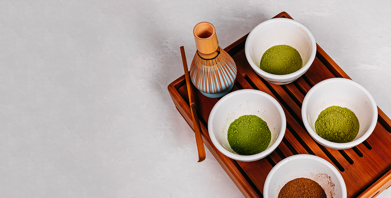 Photo of matcha whisk and four different bowls of matcha powder in varying shades