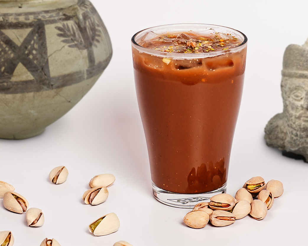 Iced mocha in a clear glass, garnished with crushed pistachios and styled with stone textures.