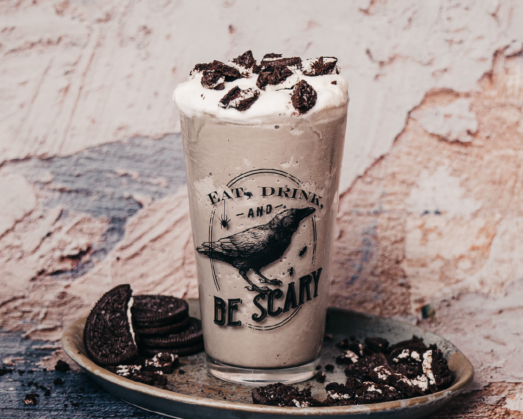 Cookies-and-cream style frappe topped with whipped cream and cookie crumbles in a gothic-themed glass.