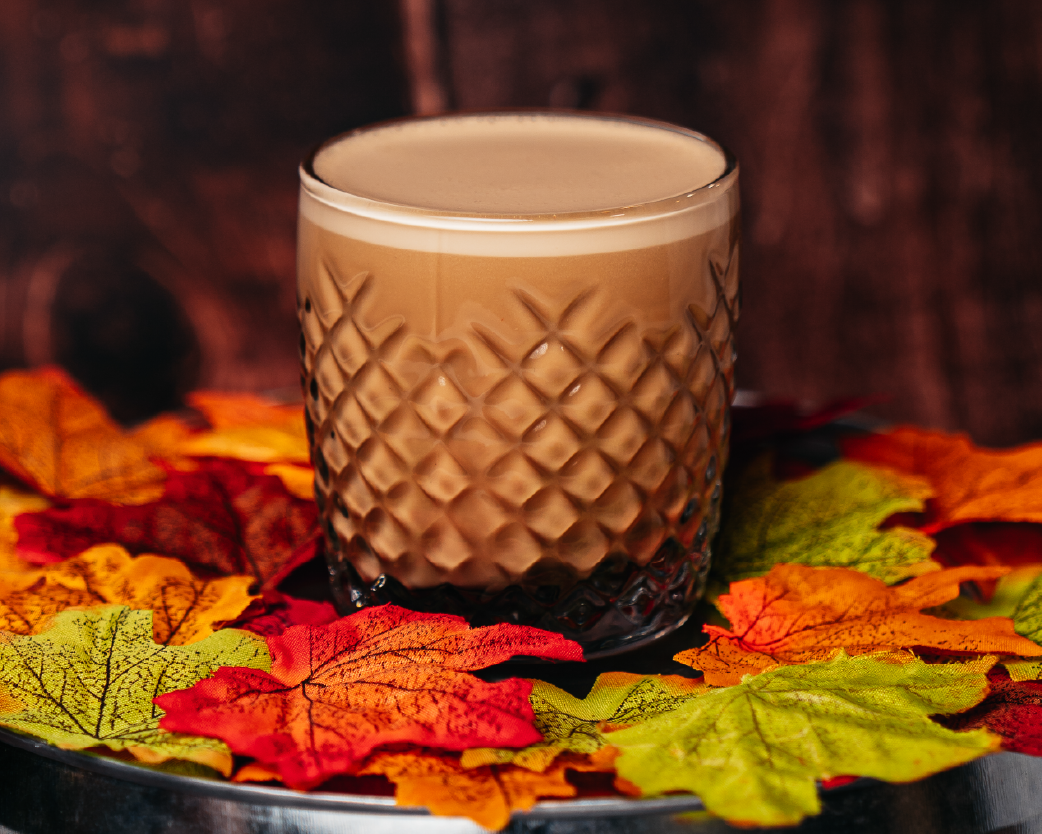 Creamy nitro-style latte in a textured glass, surrounded by fall leaves and warm autumn tones.
