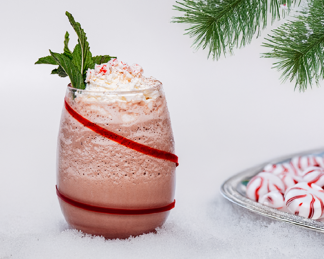 Blended chocolate drink topped with whipped cream and peppermint pieces, styled on a snowy white surface.