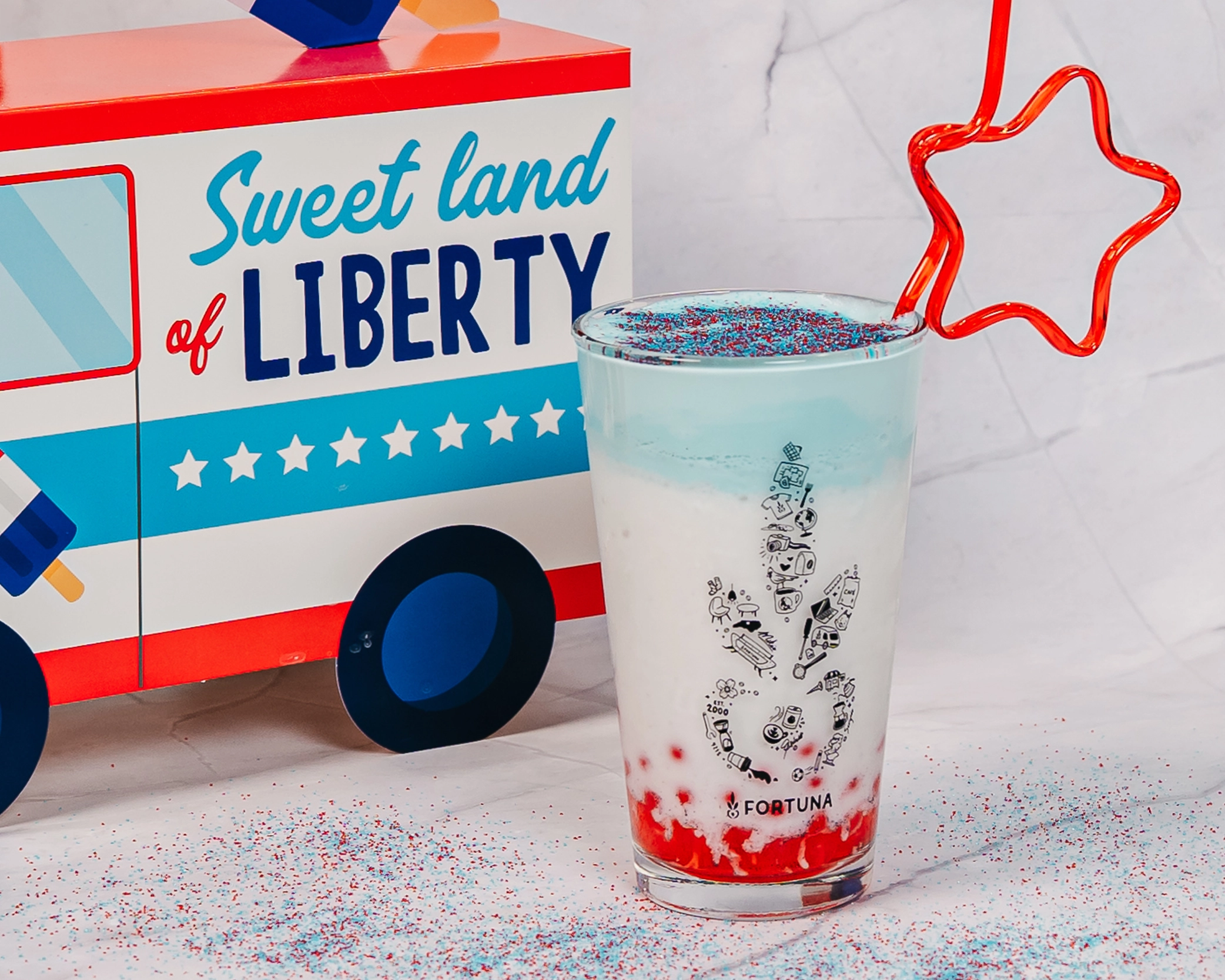 Red, white, and blue frozen drink topped with blue cold foam and patriotic sprinkles, served in a pint glass with red popping pearls in the bottom.