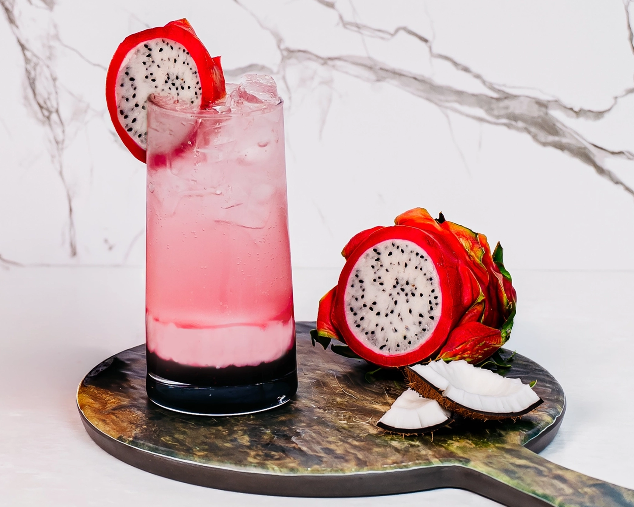 A tall glass of a layered pink dragon fruit dirty soda served over ice, garnished with a slice of dragon fruit.