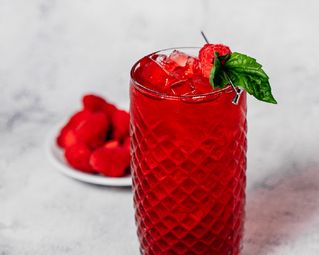 Iced raspberry tea in a clear glass with fresh raspberry and mint garnish.