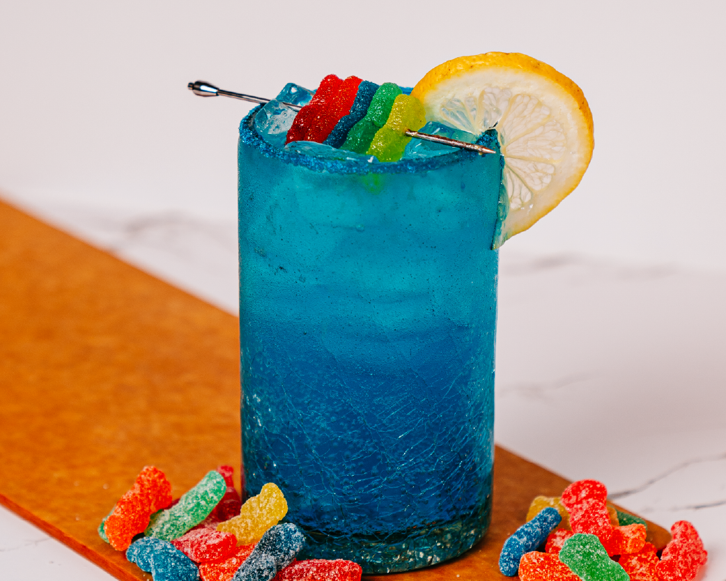 Vibrant blue iced beverage garnished with candy and citrus, styled with colorful candy accents.