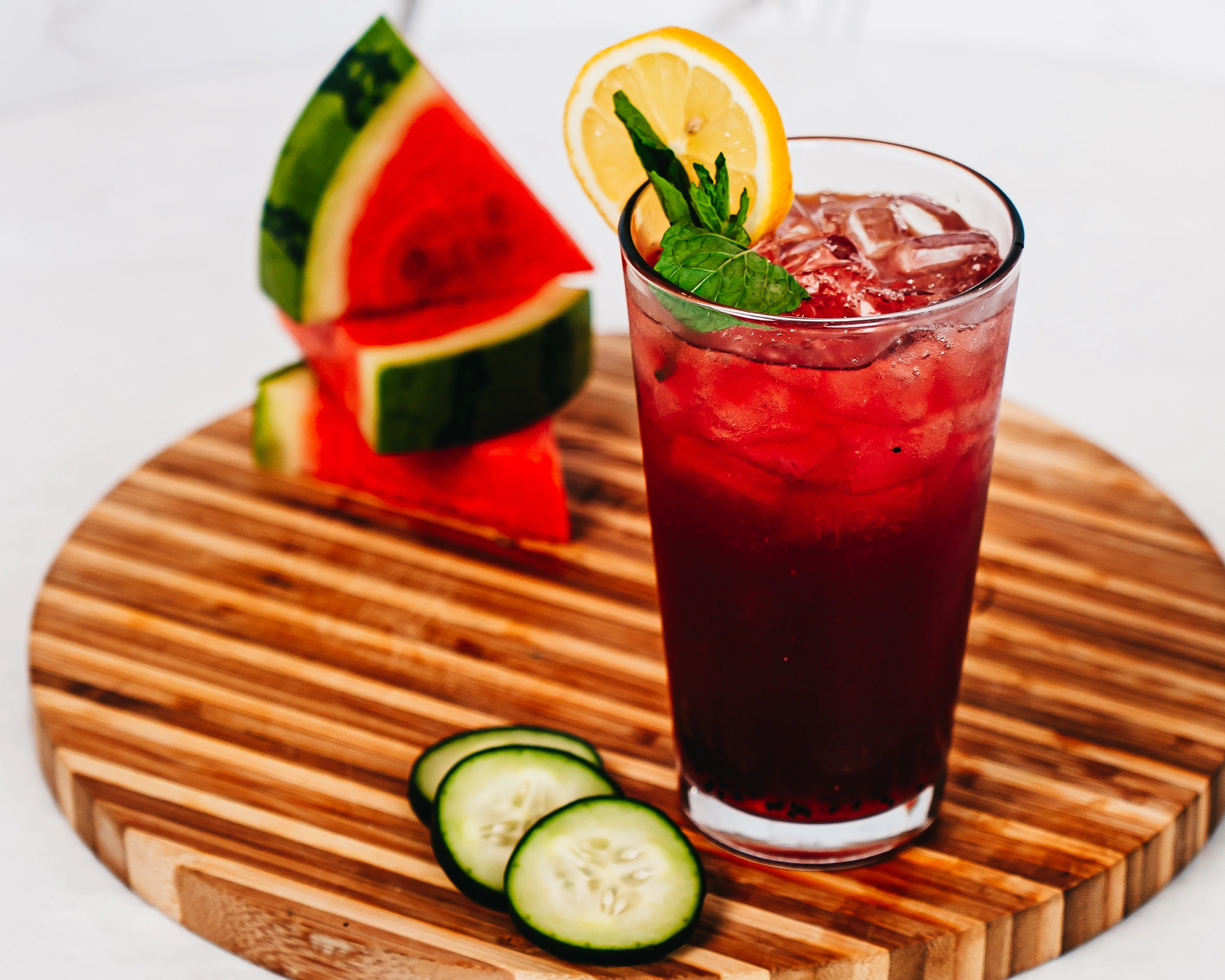 A watermelon and cucumber lemonade served in a pint glass over ice, garnished with mint and lemon slice.