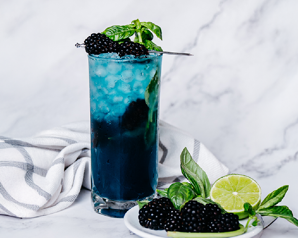 Dark berry soda with basil leaves and ice in a clear glass.